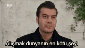 a man in a black coat is standing in front of a brick wall with a caption in a foreign language .