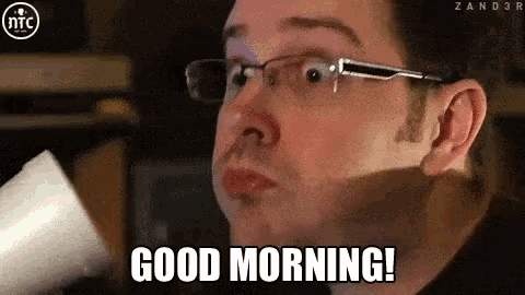a man wearing glasses says good morning while holding a cup