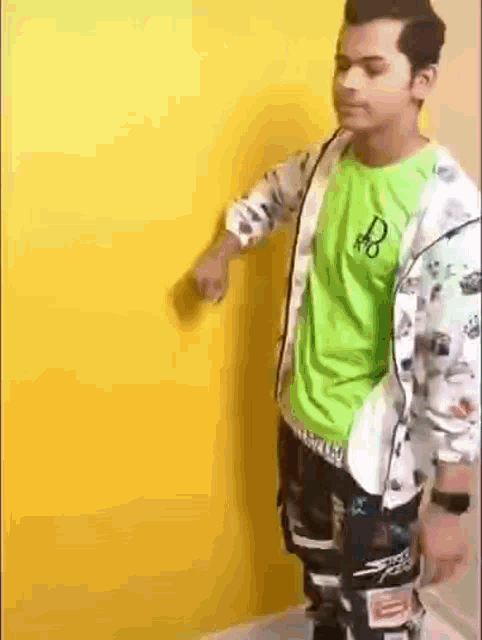 a man in a green shirt is standing in front of a yellow wall .