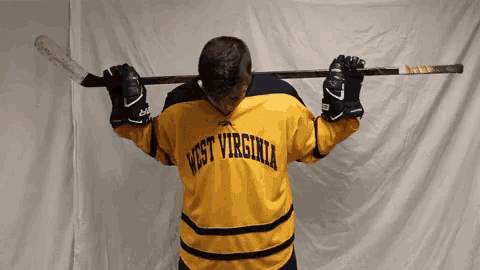 a man wearing a yellow west virginia jersey holds a hockey stick over his head