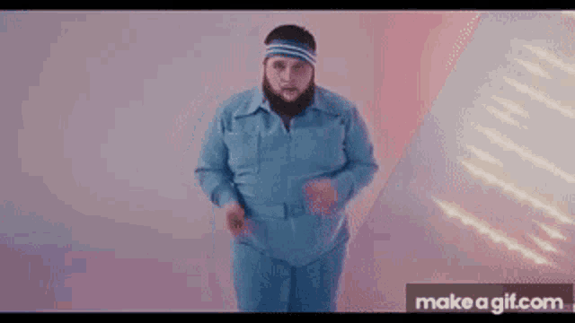 a man with a beard is wearing a blue jumpsuit and a headband while dancing .