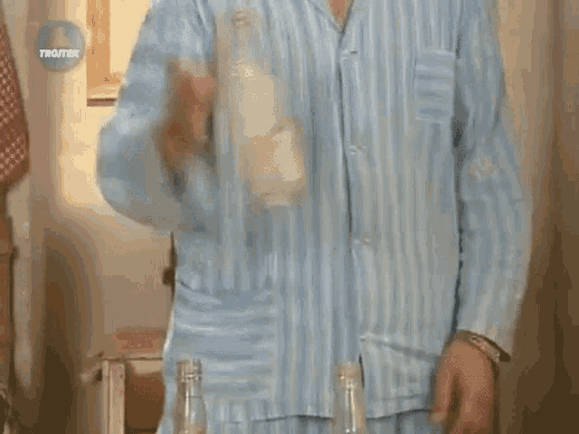 a man in a blue and white striped pajama shirt is standing in front of two bottles of water .
