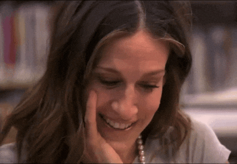 a woman wearing a pearl necklace is smiling with her hand on her face .