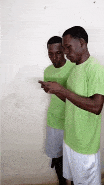 two men in green shirts and white shorts are looking at their cell phones