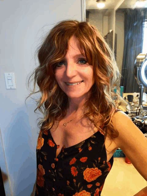 a woman with red hair and a floral top smiles for the camera