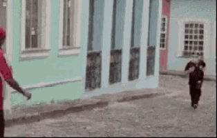 a man in a red shirt is walking down a street in front of a green building .