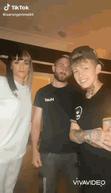 two men and a woman are posing for a picture together . one of the men is wearing a black shirt that says 19uh .
