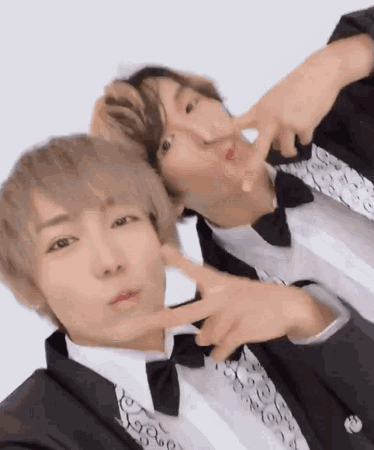two men in tuxedos are making a peace sign with their fingers