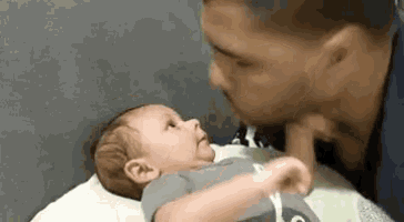 a man is kissing a baby on the cheek while laying in a crib .