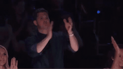 a man is clapping his hands in the air while sitting in a crowd .