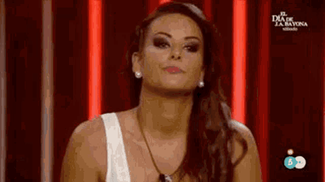 a woman in a white tank top is standing in front of a red background .