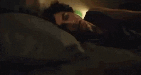 a man is laying on a bed with his eyes closed and his head on a pillow .