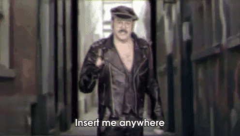 a man in a leather jacket and hat is walking down an alleyway and saying insert me anywhere .