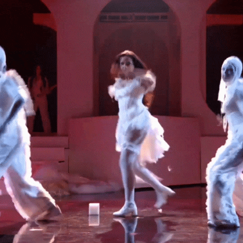 a woman in a white dress is dancing on a stage with a group of white people