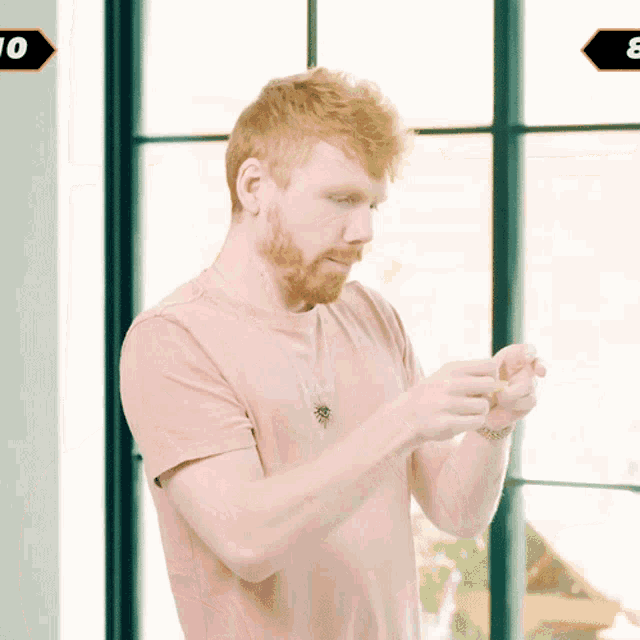 a man in a pink t-shirt is standing in front of a window with the number 10 in the corner