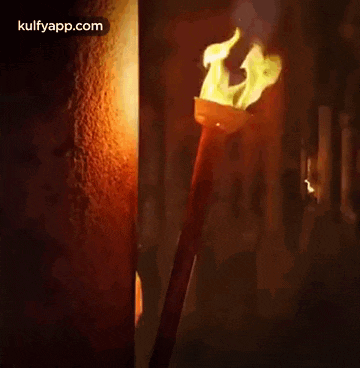 a man is peeking out from behind a wall holding a lit torch .
