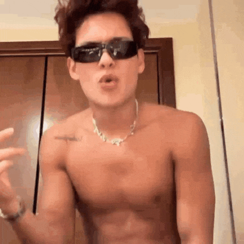 a shirtless young man wearing sunglasses and a necklace is making a funny face .