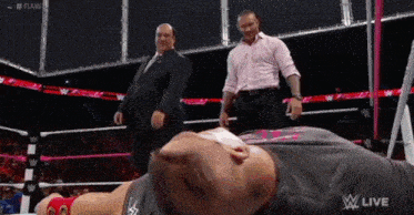 a man is laying on the ground in a wrestling ring while a referee watches .