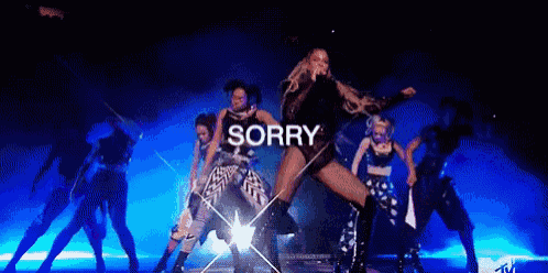 a woman is singing into a microphone while dancing on a stage with the word sorry written above her .