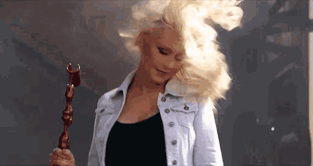 a woman in a white denim jacket is holding a wooden stick in her hand .