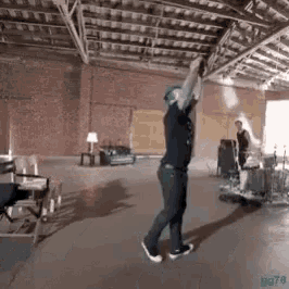 a man is dancing in a room with a brick wall and a drum set .