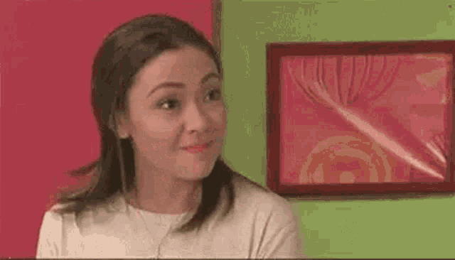 a woman is making a funny face while sitting in front of a framed picture on a wall .