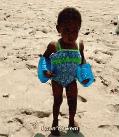 a little girl wearing a bathing suit and armbands on the beach says i can 't swim