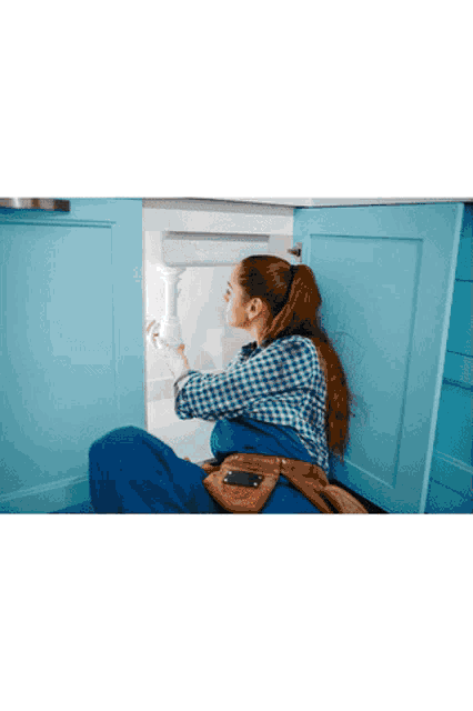 a woman is kneeling under a sink and looking at it