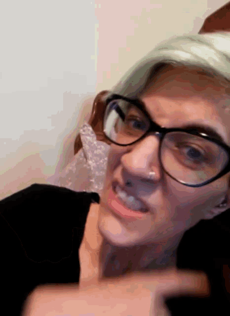 a woman with glasses and a nose ring is pointing at something