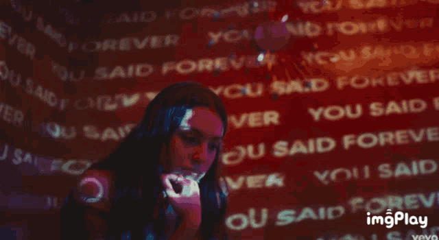 a woman stands in front of a wall that says ' you said forever '