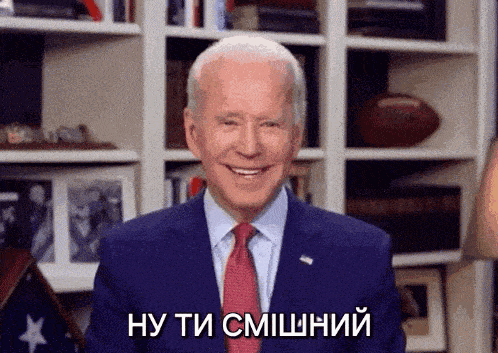 a man in a suit and tie is smiling in front of a bookshelf and says ну ти смішний