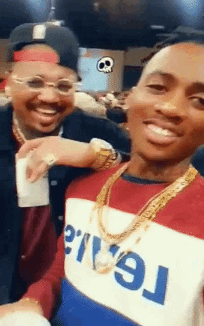two men are posing for a picture and one of them is wearing a sweater that says ' real ' on it