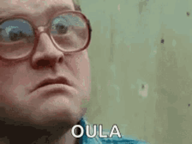 a man wearing glasses and a blue shirt is making a funny face and saying oula .
