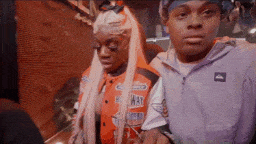 a man and a woman are standing next to each other and the woman is wearing an orange jacket with the word highway on it