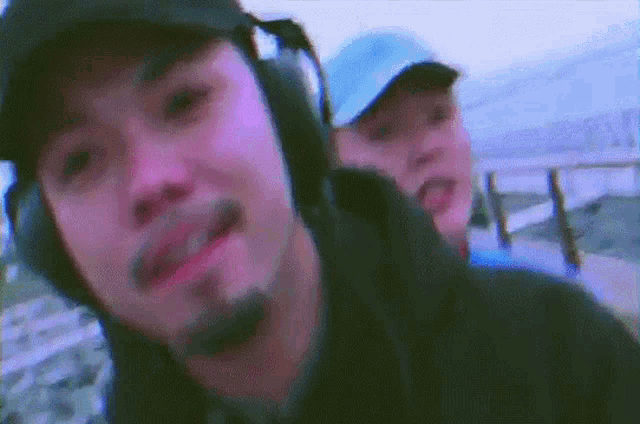 a man with a beard wearing headphones stands next to another man