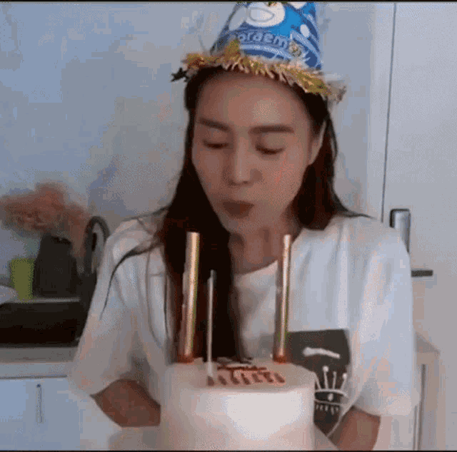 a woman is blowing out candles on a birthday cake while wearing a party hat .