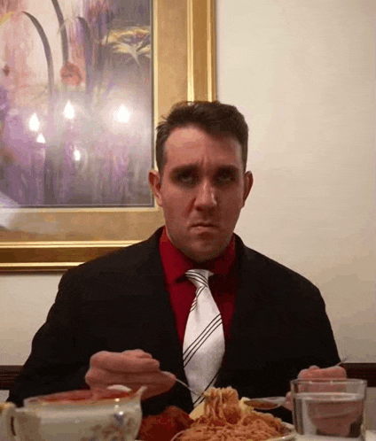 a man wearing a suit and tie is eating spaghetti