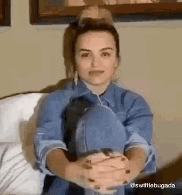 a woman in a blue shirt is sitting on a couch with her legs crossed .