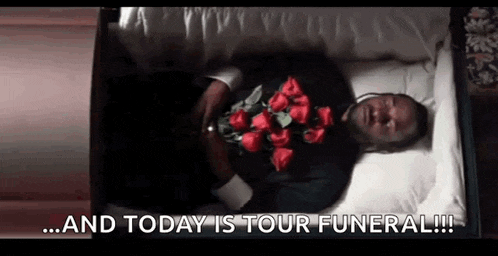 a man is laying in a coffin with a bouquet of red roses on his chest .