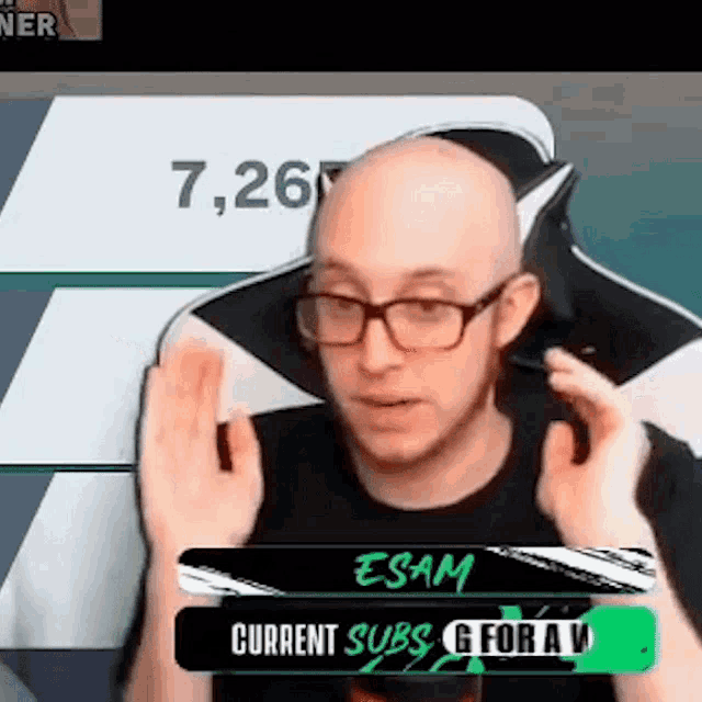 a bald man wearing glasses and a black shirt is sitting in a chair with a sign that says current subs
