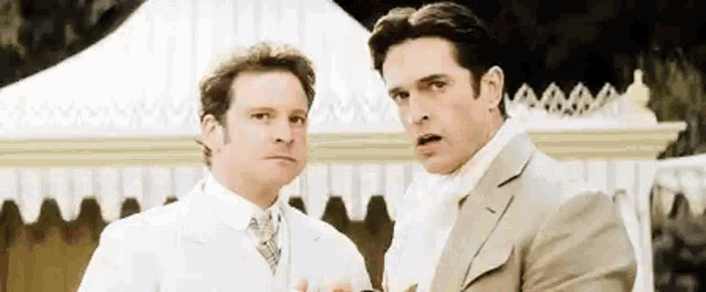 two men in suits are standing next to each other in front of a white tent .
