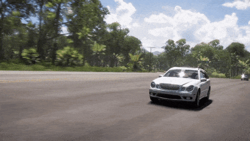a white car is driving down a road with trees on the side of it