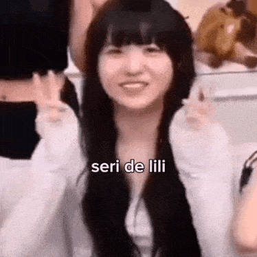 a girl with long black hair is giving a peace sign while sitting in front of a group of people .