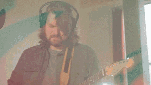 a man with a beard is playing a guitar in a room with a window .