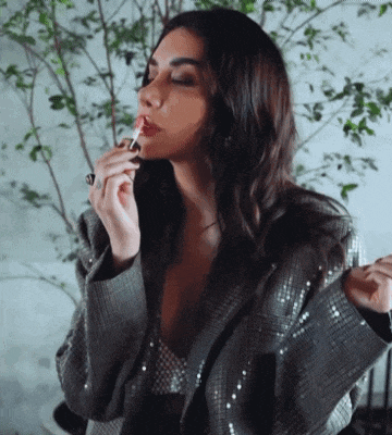 a woman is applying lipstick to her lips while wearing a sequined jacket