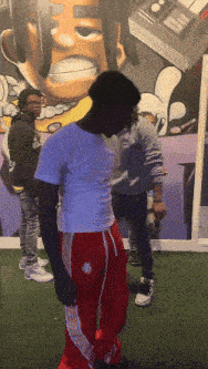 a man in a white shirt and red pants is standing in front of a wall with a cartoon character on it
