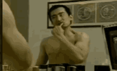 a shirtless man is shaving in front of a mirror in a bathroom .