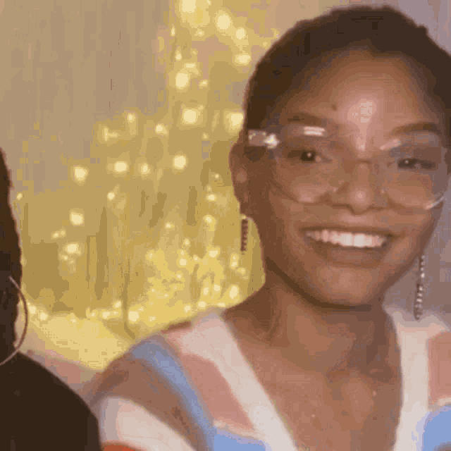 a woman wearing glasses and earrings smiles for the camera .