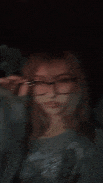 a girl wearing glasses and a gray shirt is taking a selfie