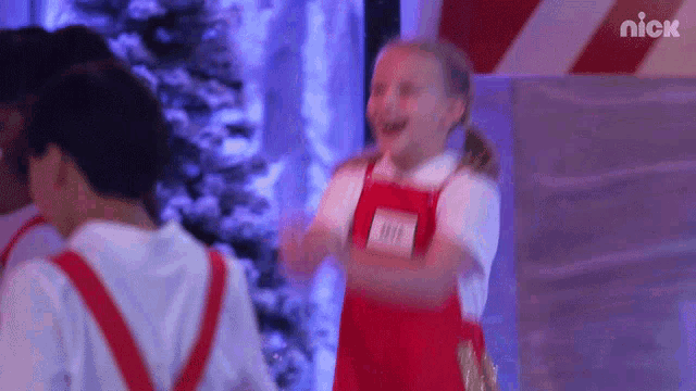 a girl wearing red overalls has a nick name tag on her chest